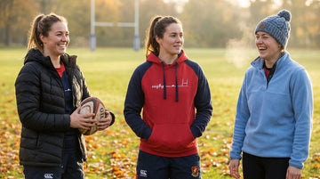 Athletic women teammates layered in warm game day layers on outdoor rugby pitch sideline