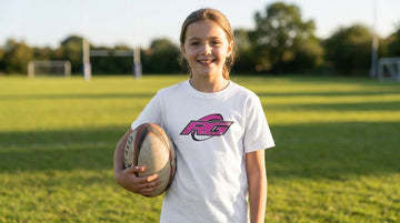 Young girl on rugby pitch wearing white RG Impact kids rugby shirt holding ball