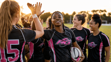 Female rugby players celebrating together on field in warm sunlight
