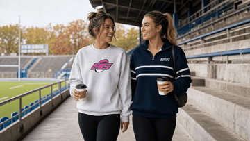 Two female rugby fans in stadium bleachers wearing best game day sweatshirts for rugby fans on chilly morning