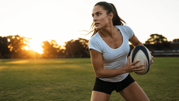 Woman holding a rugby ball on a field at golden hour