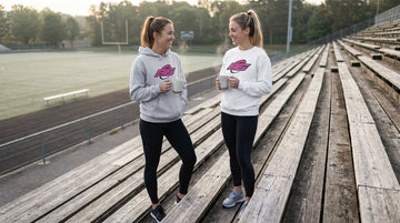 Two women comparing rugby hoodie versus sweatshirt with RG Impact graphics on bleachers