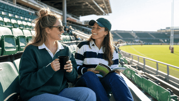 Two women rugby supporters holding ceramic mug on stadium bleachers before match kickoff