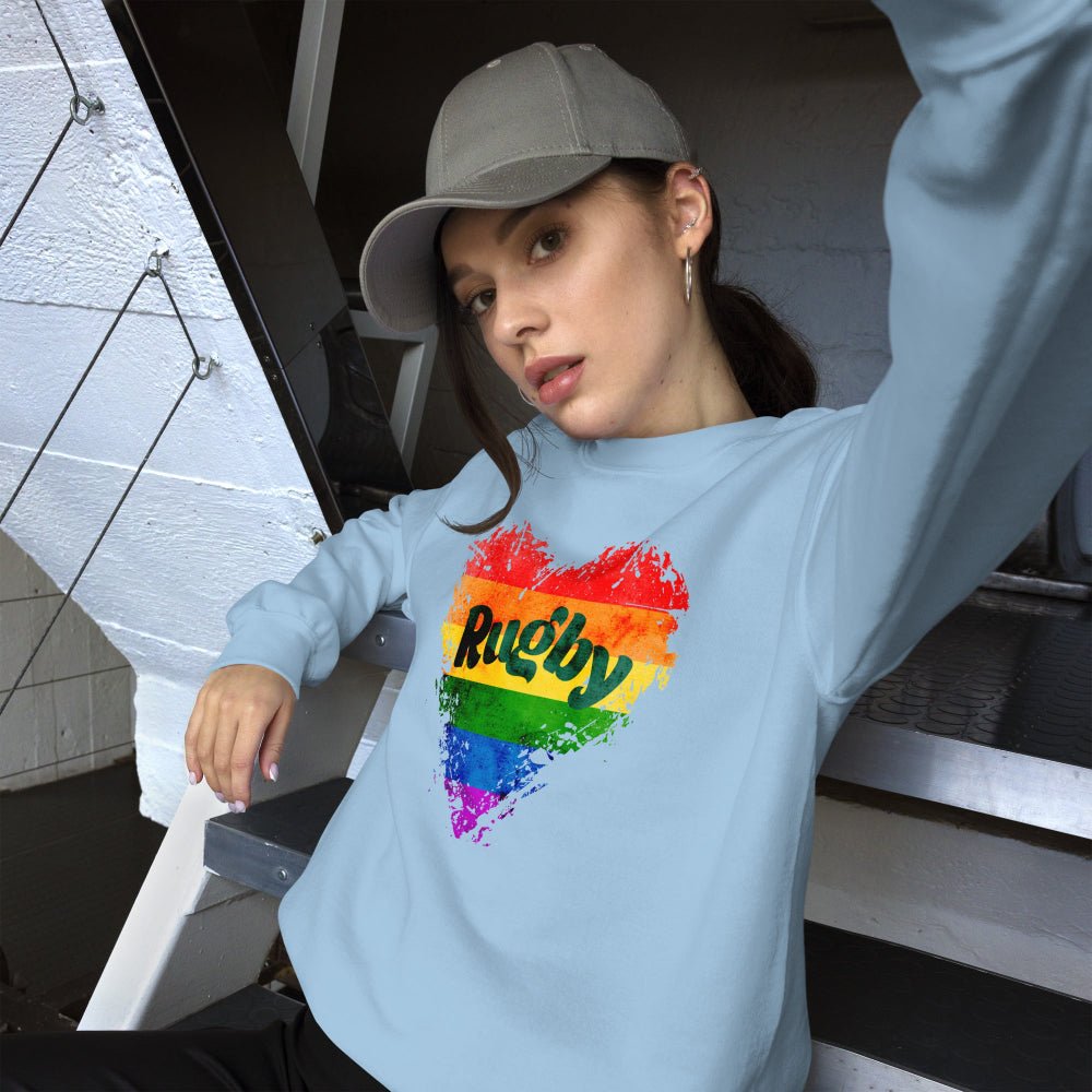 Light blue women's rugby sweatshirt with rainbow heart and bold "Rugby" text, paired with gray cap. - Rugby Girl